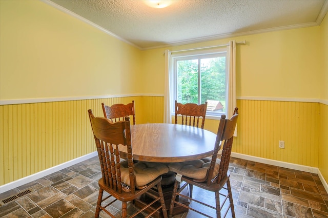 dining space featuring wood walls, crown molding, and a textured ceiling