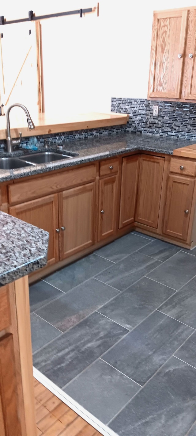 kitchen featuring decorative backsplash, a barn door, dark stone counters, and sink