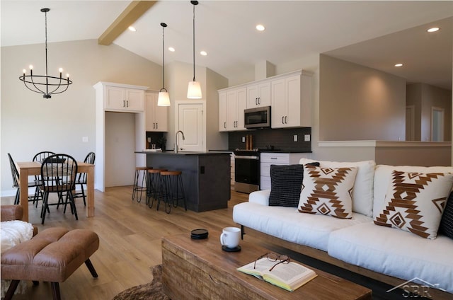 living room featuring vaulted ceiling with beams, light hardwood / wood-style floors, an inviting chandelier, and sink