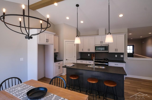 kitchen featuring white cabinets, decorative backsplash, an island with sink, appliances with stainless steel finishes, and dark hardwood / wood-style flooring