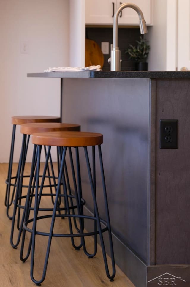 bar with white cabinets and light hardwood / wood-style flooring