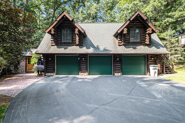 11245 Guyn Dr, Brighton, MI 48114 - log cabin featuring log exterior, driveway, an attached garage, stairs, and roof with shingles