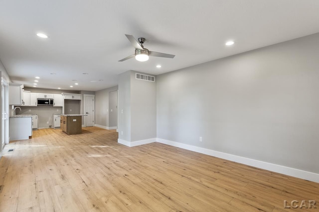 unfurnished living room featuring light hardwood / wood-style flooring, ceiling fan, and sink