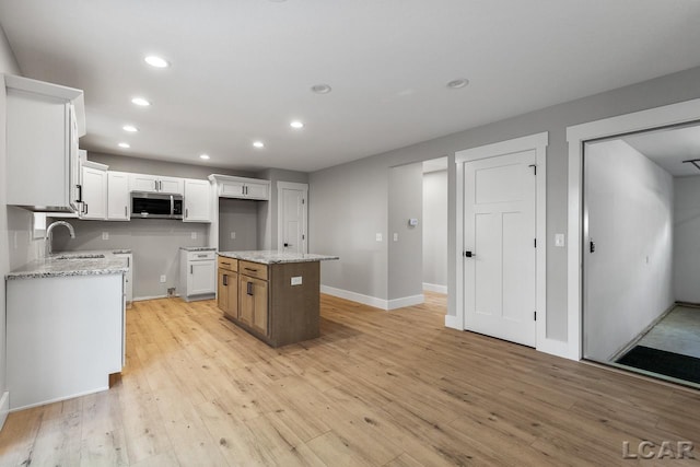 kitchen with light stone countertops, light wood-type flooring, sink, white cabinets, and a kitchen island