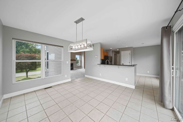 interior space with stainless steel refrigerator, kitchen peninsula, light tile patterned flooring, and pendant lighting