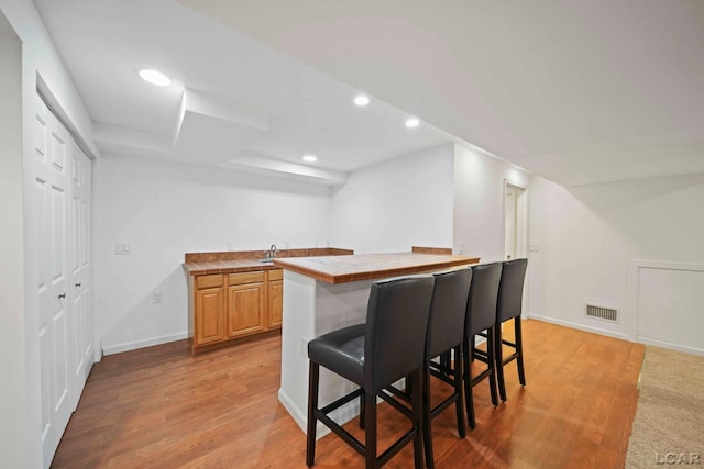 kitchen with sink, tile counters, light brown cabinets, a breakfast bar area, and light wood-type flooring