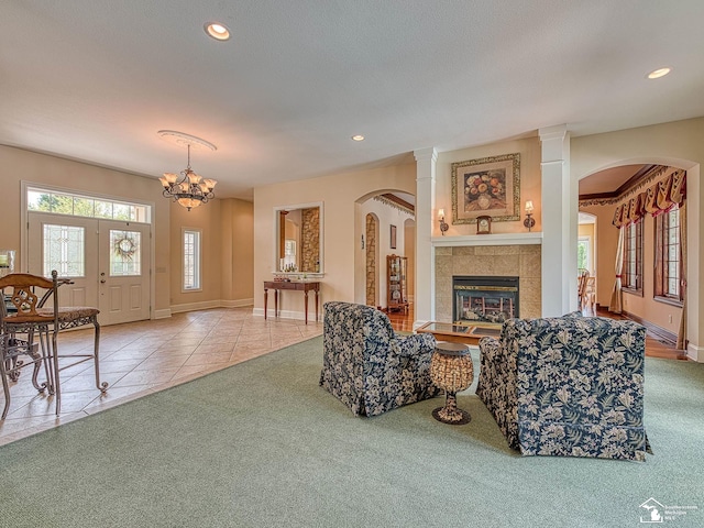 living room with light carpet, an inviting chandelier, a tiled fireplace, a textured ceiling, and decorative columns