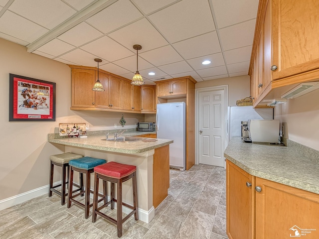 kitchen with a kitchen breakfast bar, a drop ceiling, sink, decorative light fixtures, and white fridge