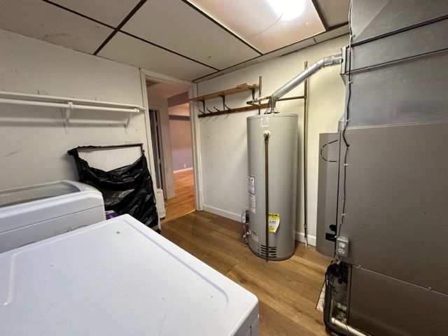 basement with heating unit, water heater, hardwood / wood-style floors, and washer / dryer