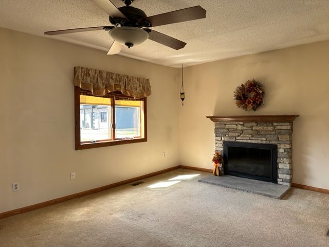 unfurnished living room with carpet flooring, a stone fireplace, ceiling fan, and a textured ceiling