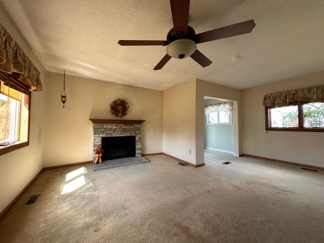 unfurnished living room featuring carpet flooring, a stone fireplace, a healthy amount of sunlight, and a textured ceiling