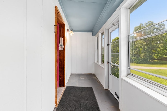 hallway featuring wooden walls, a healthy amount of sunlight, and ornamental molding