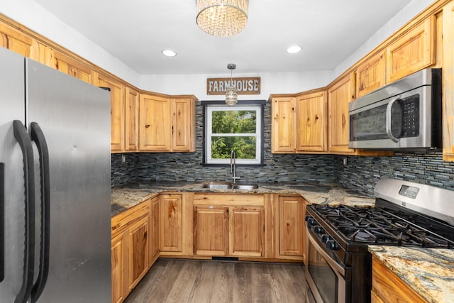 kitchen with sink, dark wood-type flooring, stainless steel appliances, light stone counters, and decorative light fixtures