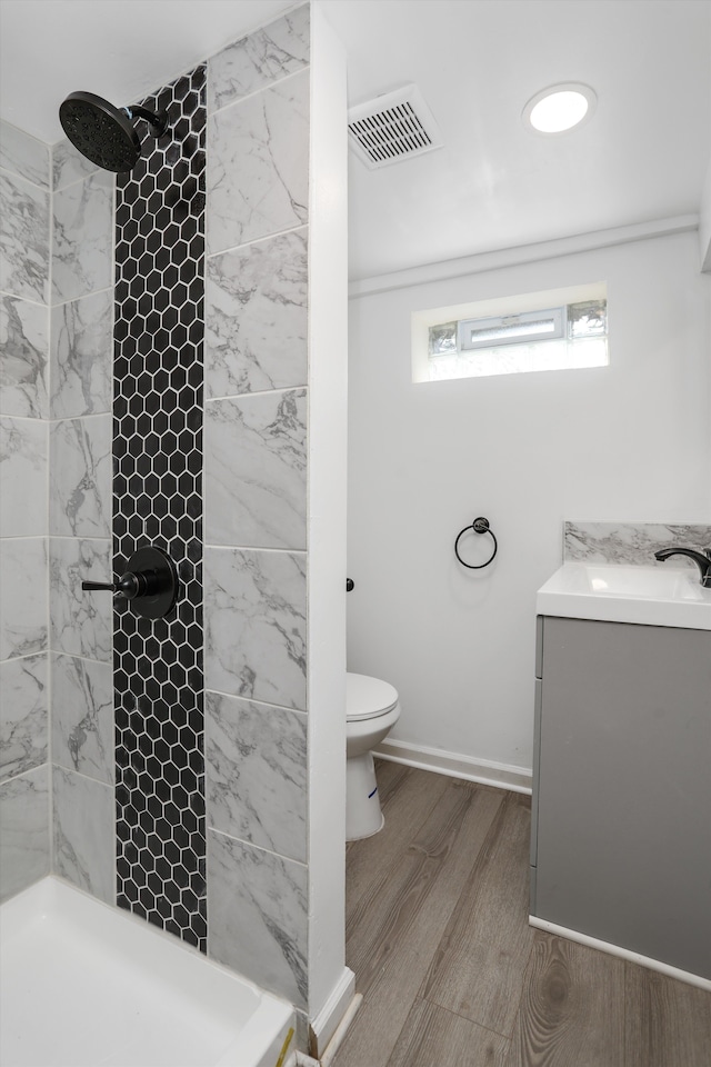 bathroom featuring a tile shower, hardwood / wood-style floors, vanity, and toilet