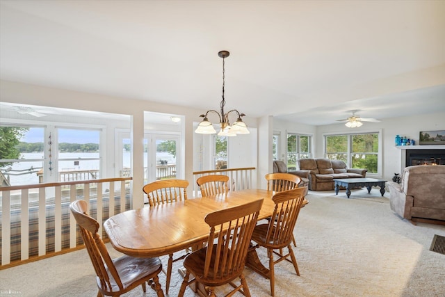 carpeted dining room with a water view and ceiling fan with notable chandelier