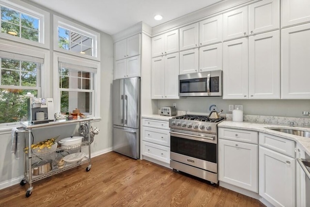 kitchen with light stone countertops, white cabinetry, sink, light hardwood / wood-style floors, and appliances with stainless steel finishes