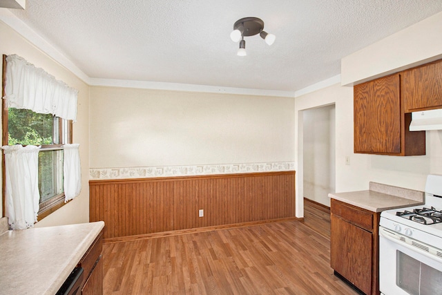 kitchen with light wood-type flooring, a textured ceiling, range hood, and gas range gas stove