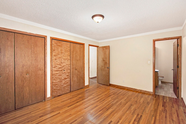 unfurnished bedroom with ensuite bathroom, two closets, a textured ceiling, and light hardwood / wood-style flooring