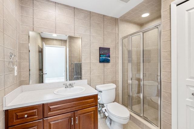 bathroom featuring vanity, a shower with shower door, tile walls, and toilet