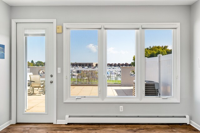 doorway with plenty of natural light, wood-type flooring, and a baseboard heating unit