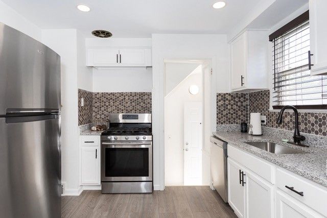 8410 Grandville Ave, Detroit, MI 48228 - kitchen with appliances with stainless steel finishes, a sink, wood finished floors, tasteful backsplash, and white cabinets