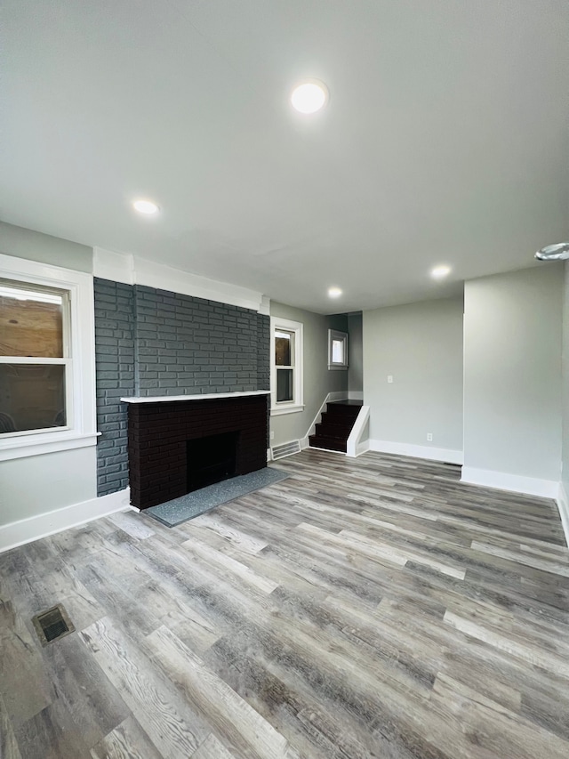 unfurnished living room with hardwood / wood-style flooring and a brick fireplace