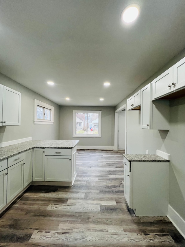 kitchen featuring hardwood / wood-style floors, light stone countertops, white cabinetry, and kitchen peninsula