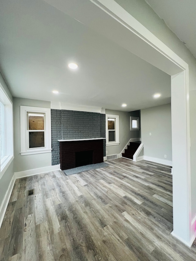 unfurnished living room featuring hardwood / wood-style floors and a brick fireplace