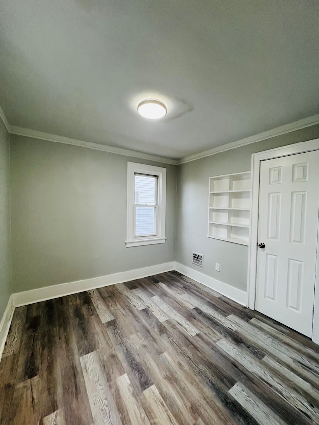 spare room with built in features, ornamental molding, and dark wood-type flooring