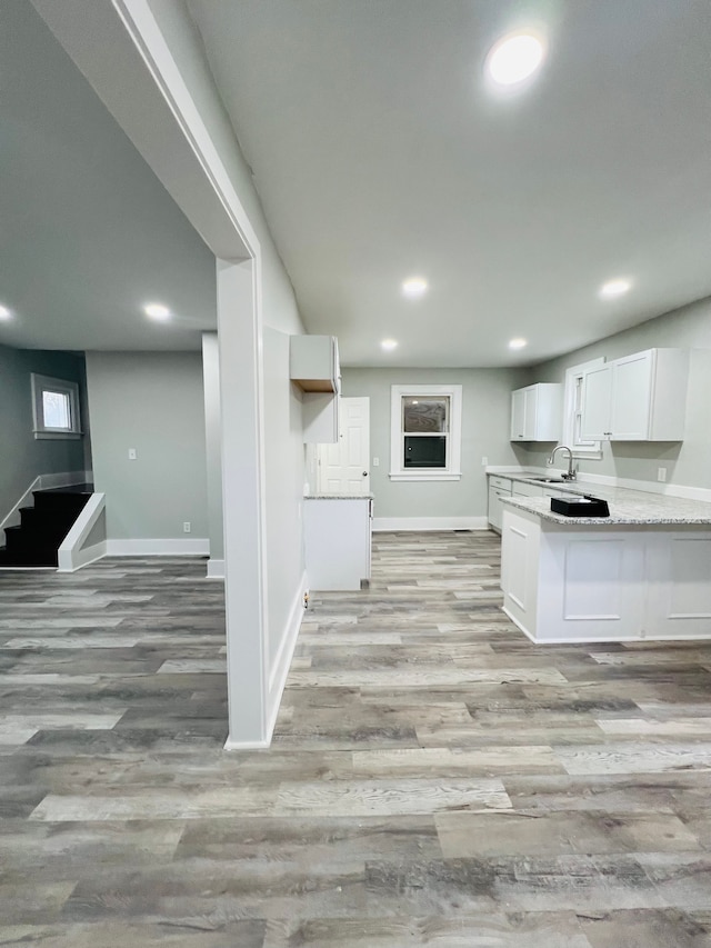 kitchen with kitchen peninsula, light wood-type flooring, white cabinetry, and sink