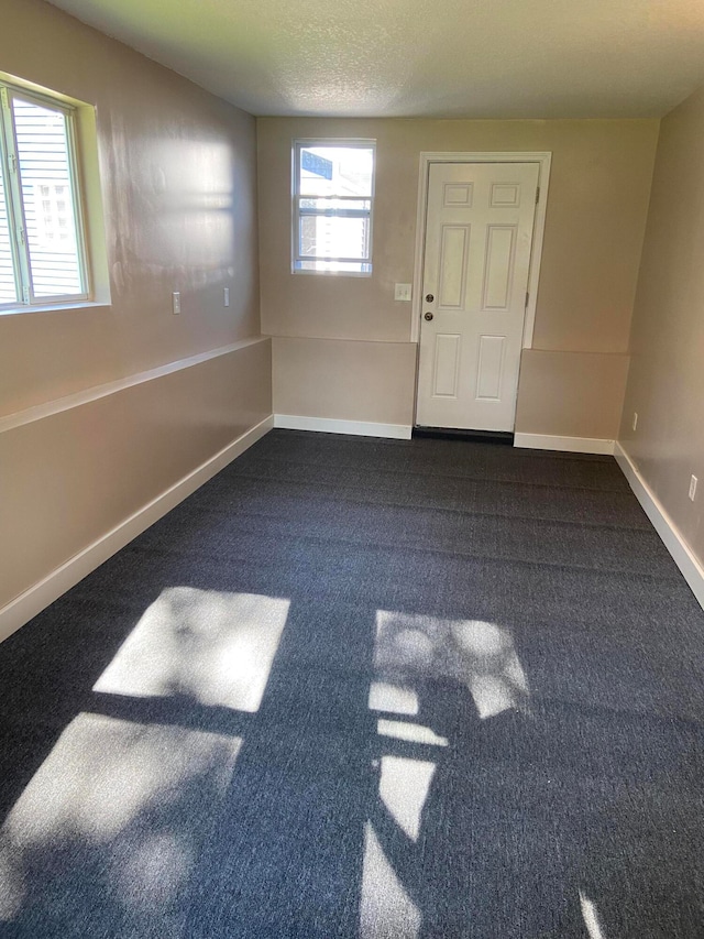 spare room with baseboards, dark colored carpet, and a textured ceiling