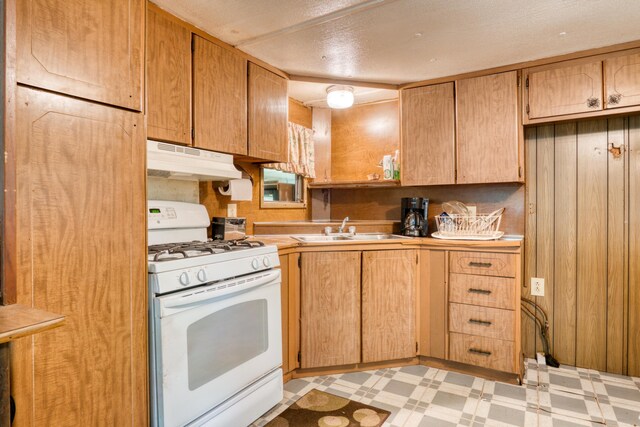 11451 Hemlock Ave, Lake, MI 48632 - kitchen with white gas stove, under cabinet range hood, a sink, light floors, and light countertops