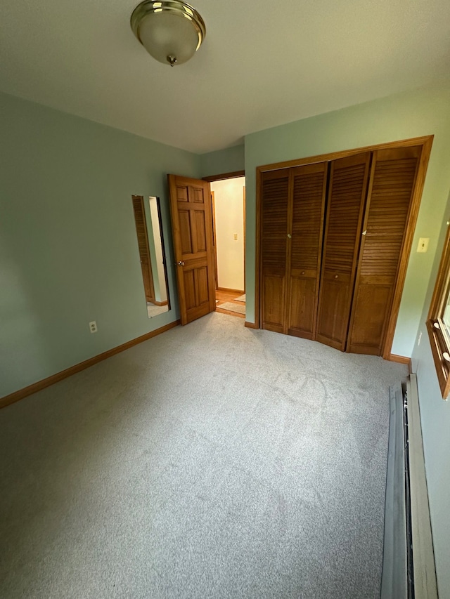 unfurnished bedroom with baseboard heating, light carpet, and a closet