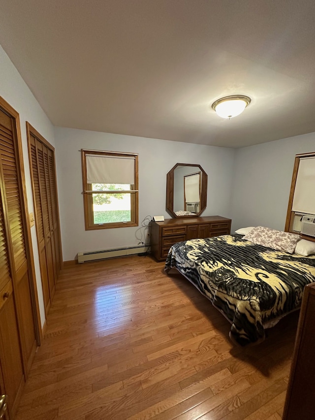 bedroom featuring multiple closets, light wood-type flooring, and a baseboard heating unit