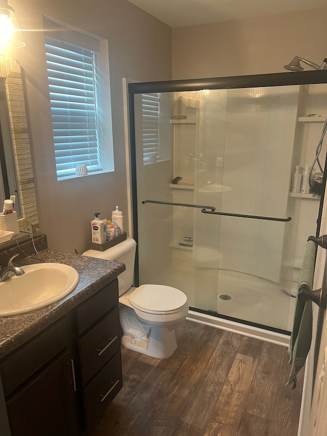 bathroom with hardwood / wood-style floors, vanity, toilet, and a shower with door