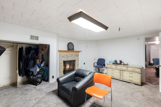 sitting room featuring a stone fireplace and light carpet