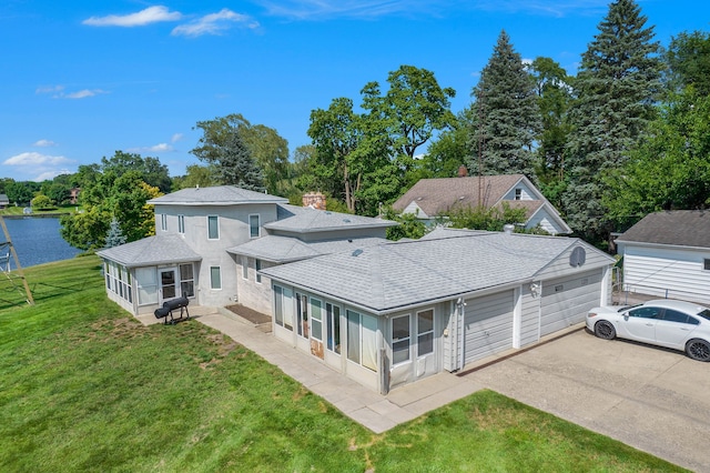 back of property featuring a sunroom, a water view, a garage, and a lawn