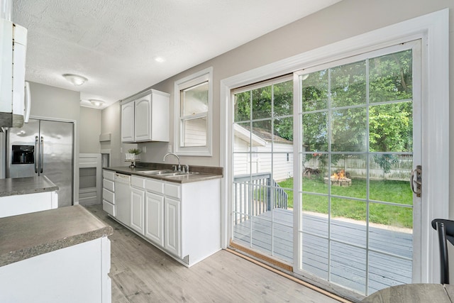 kitchen with stainless steel fridge, a wealth of natural light, white cabinetry, and light hardwood / wood-style flooring