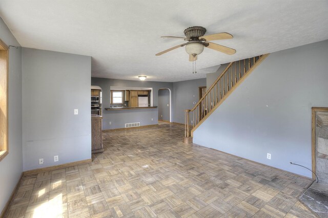 20682 Honor Hwy, Interlochen, MI 49643 - unfurnished living room featuring ceiling fan, arched walkways, stairs, baseboards, and a textured ceiling