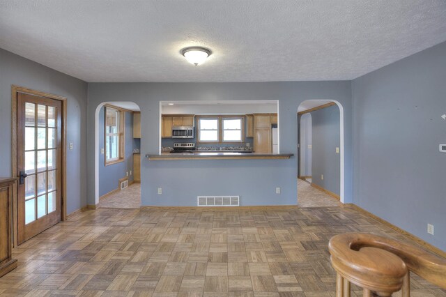 20682 Honor Hwy, Interlochen, MI 49643 - kitchen featuring stainless steel appliances, arched walkways, baseboards, a textured ceiling, and a peninsula