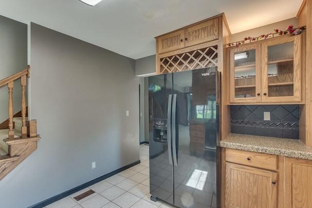 kitchen featuring light tile patterned flooring, light stone countertops, backsplash, and black refrigerator with ice dispenser