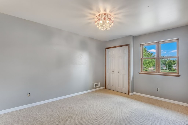 unfurnished bedroom with light carpet, a closet, and a notable chandelier