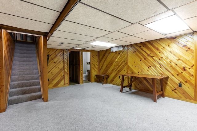 basement featuring a drop ceiling, carpet floors, and wooden walls