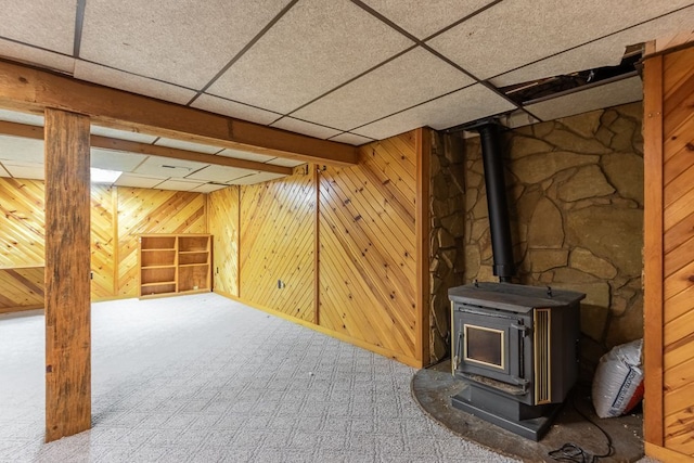 basement with a wood stove, wood walls, and a paneled ceiling