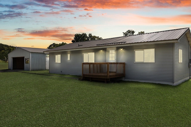 back house at dusk featuring a lawn, a garage, an outdoor structure, and a wooden deck