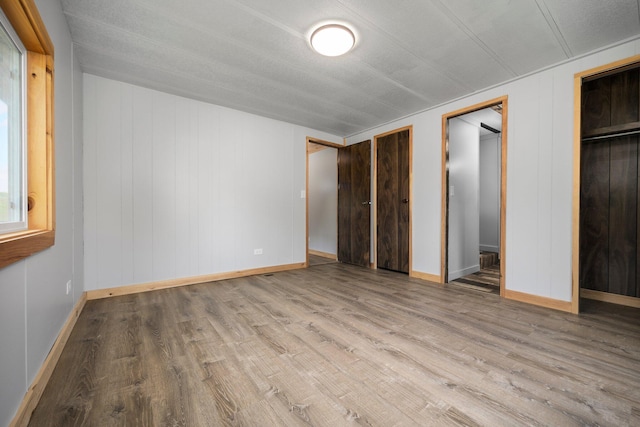 unfurnished bedroom featuring multiple closets, wood walls, light hardwood / wood-style floors, and a textured ceiling