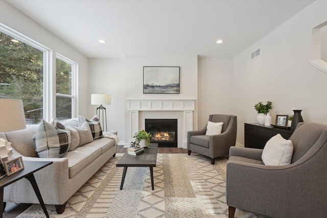 living room with light wood-style floors, a glass covered fireplace, visible vents, and recessed lighting