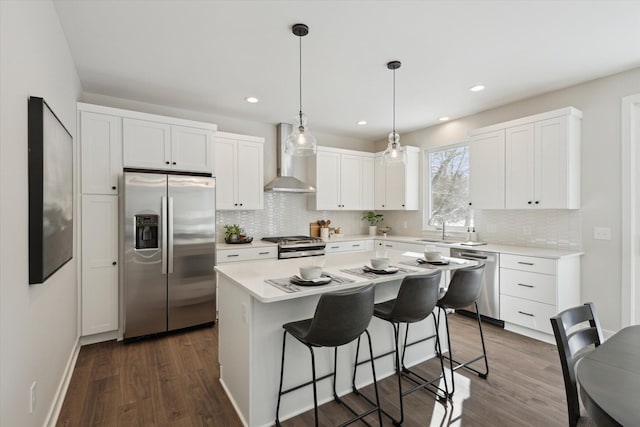 kitchen featuring white cabinets, wall chimney exhaust hood, appliances with stainless steel finishes, dark wood-style flooring, and light countertops