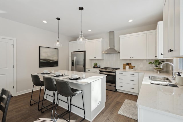 kitchen with a breakfast bar area, stainless steel appliances, a sink, decorative backsplash, and wall chimney exhaust hood