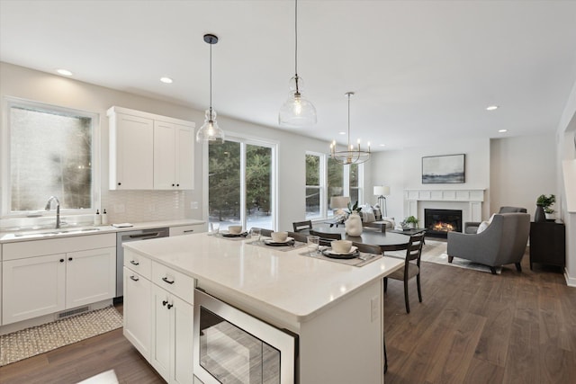 kitchen with stainless steel appliances, dark wood-type flooring, white cabinets, a sink, and a warm lit fireplace